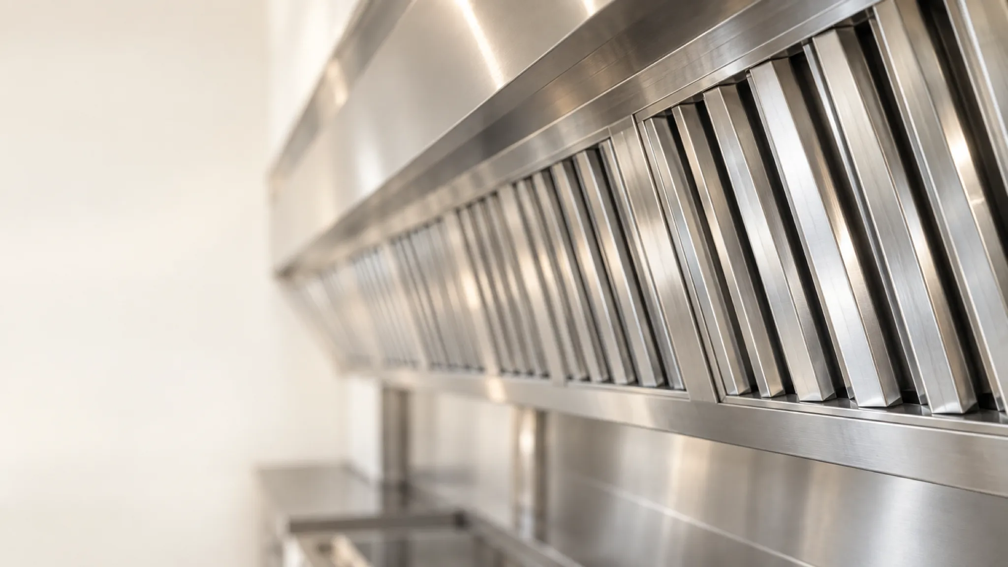 A long row of stainless baffle filters in an exhaust hood, the nearest ones sharp and gleaming